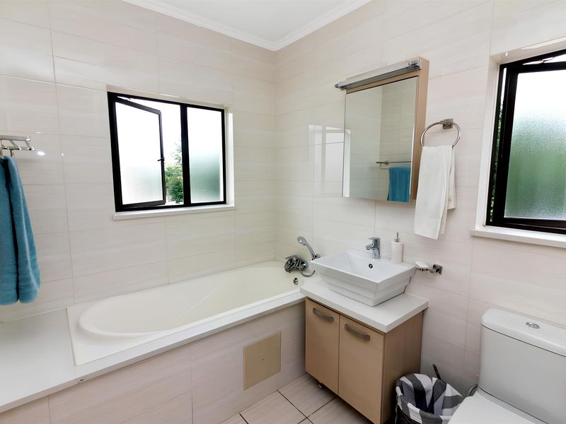 A clean, modern bathroom featuring a built-in bathtub, a vessel sink vanity, and tiled walls with two windows providing natural light.