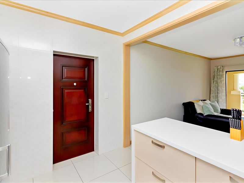 An open-plan apartment entrance area featuring tiled flooring, a solid wood front door, and a view into the adjacent living space.