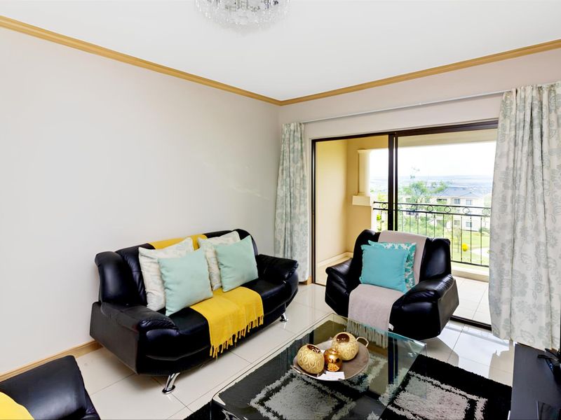 A bright living room featuring tiled flooring, crown molding, and large sliding glass doors that open onto a private balcony with scenic views.