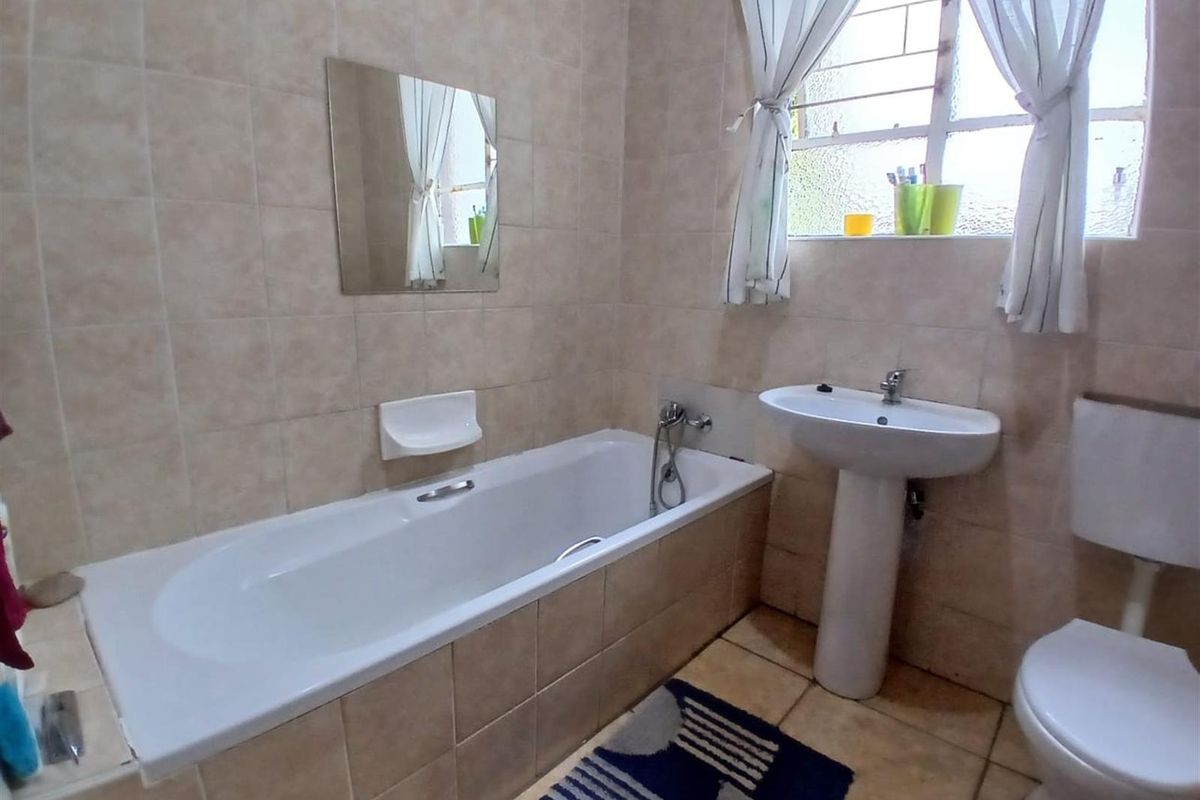 A functional bathroom featuring a built-in bathtub, pedestal basin, and toilet with neutral wall tiling and natural light from a window.
