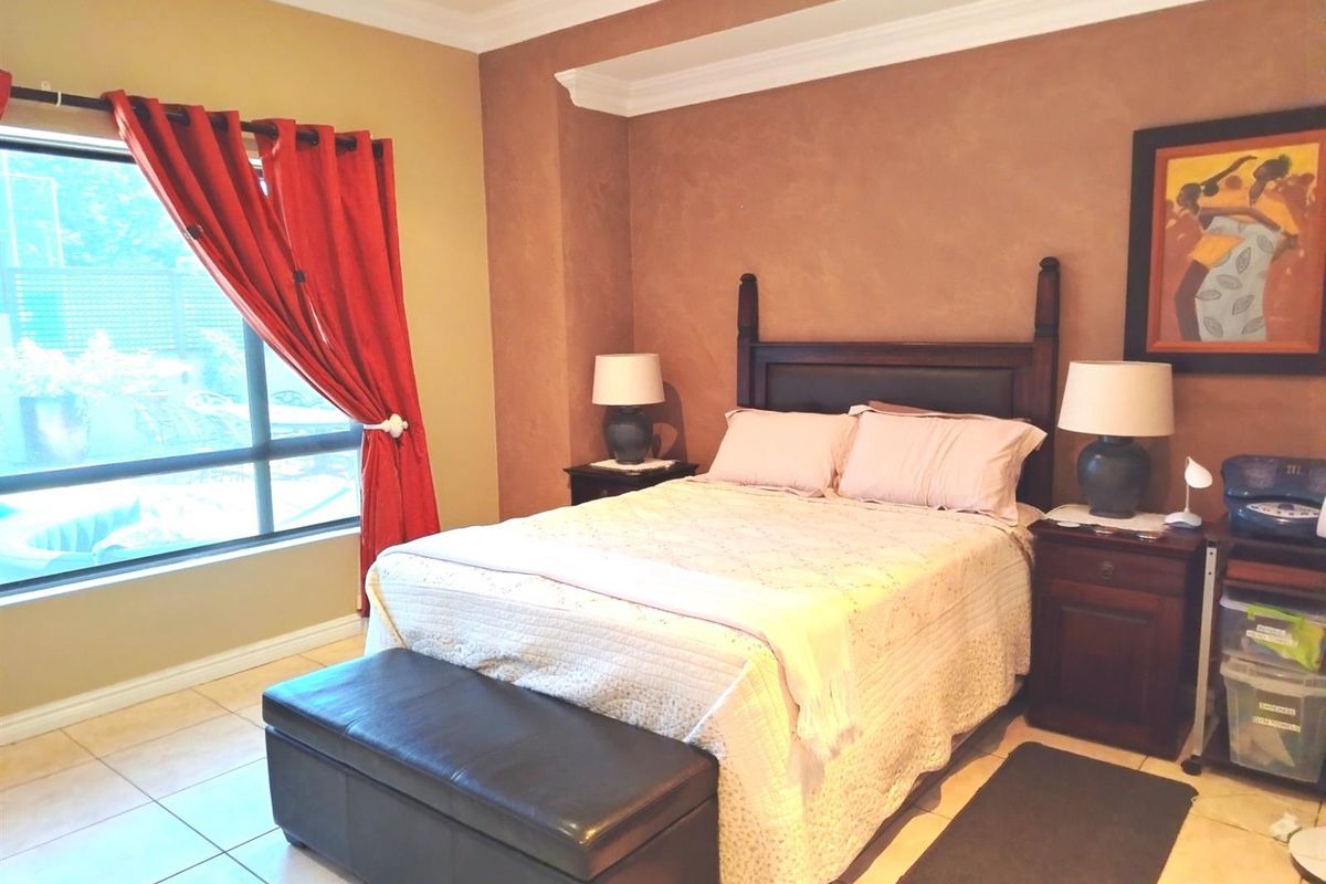 A bedroom featuring tiled flooring, crown molding, and a recessed ceiling detail, with natural light provided by a large window.
