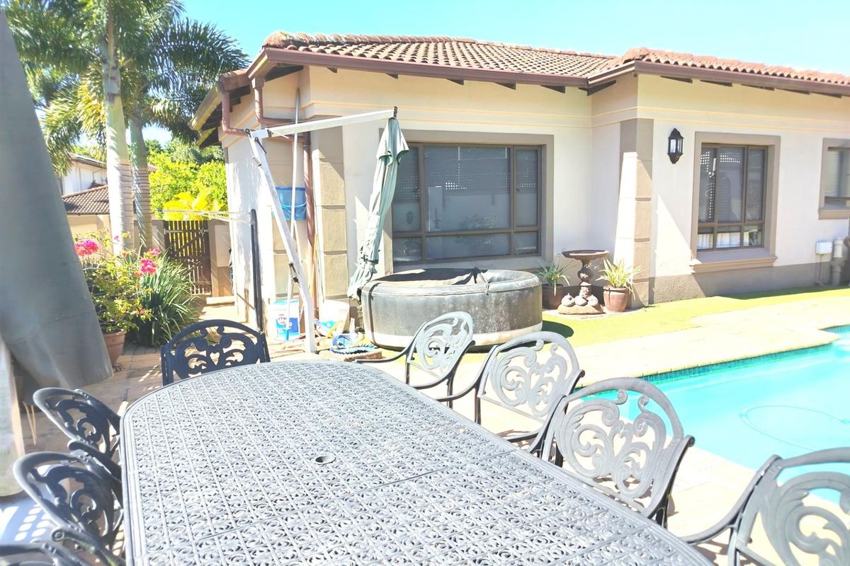 Rear exterior view of the house featuring a swimming pool, paved patio area, and tiled roof structure.
