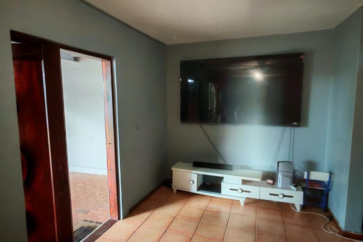 A living room featuring terracotta floor tiles and a wall-mounted television setup, with direct access to an adjacent outdoor area.