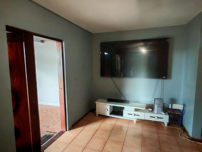 A living room featuring terracotta floor tiles and a wall-mounted television setup, with direct access to an adjacent outdoor area.