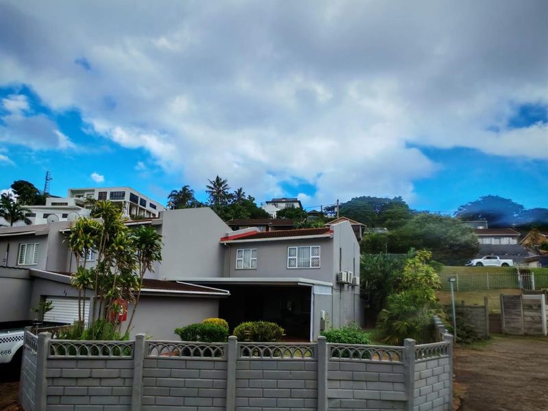 A view of the property's exterior front facade, featuring a grey rendered finish, tiled roof, and a perimeter boundary wall.