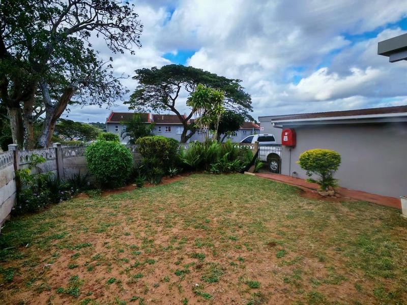 A view of the rear garden area featuring a lawn, established shrubs, and perimeter boundary walling.