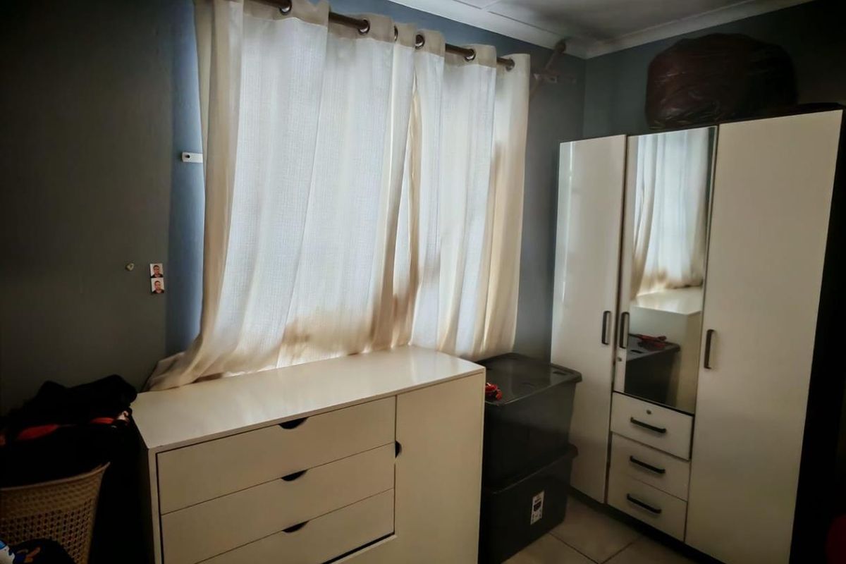 A bedroom featuring tiled flooring, a window with curtain rod, and built-in style cabinetry.