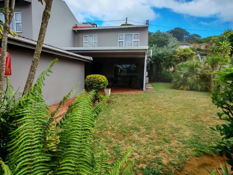 Rear view of the property featuring a covered patio area, landscaped garden, and established greenery.