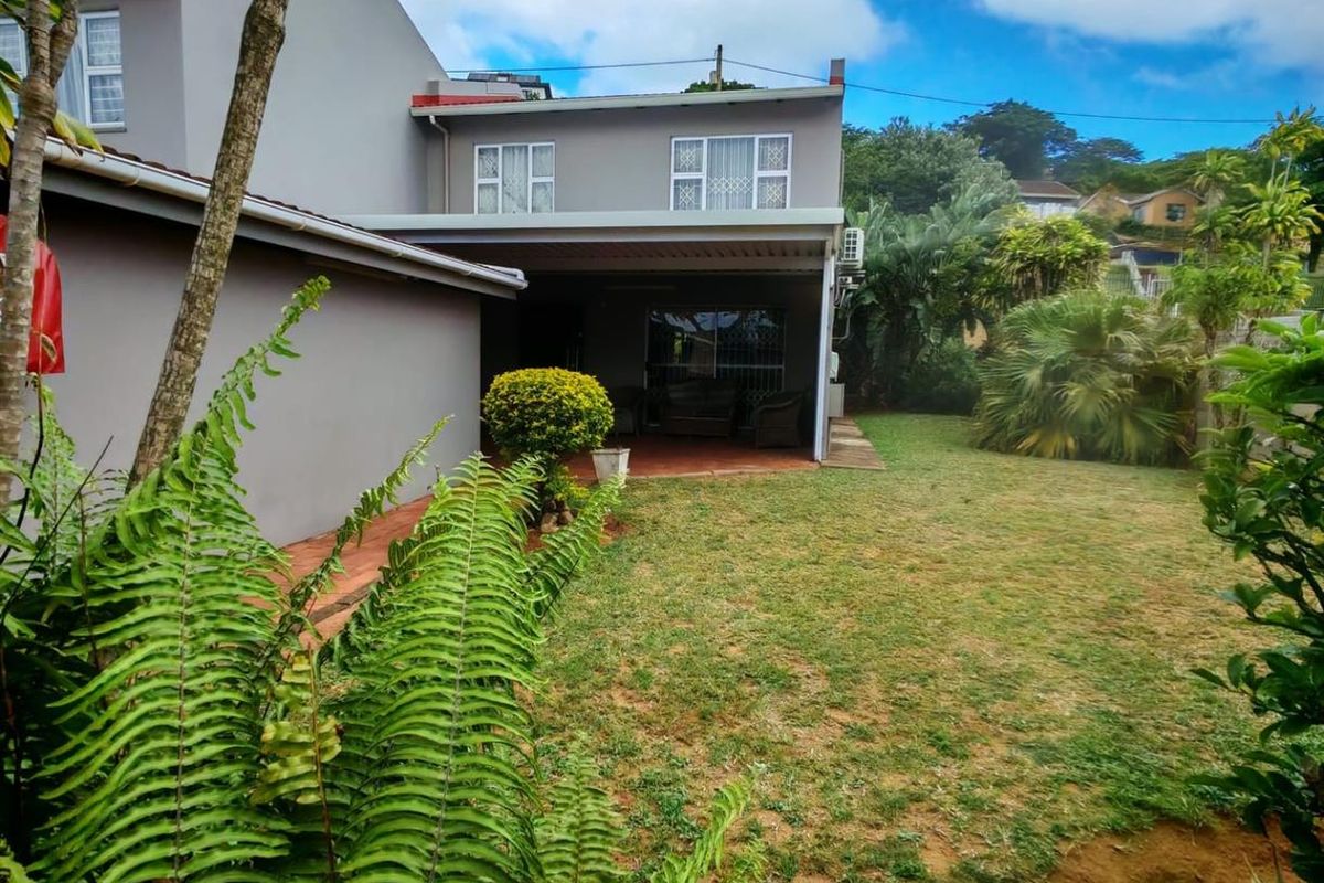 Rear view of the property featuring a covered patio area, landscaped garden, and established greenery.
