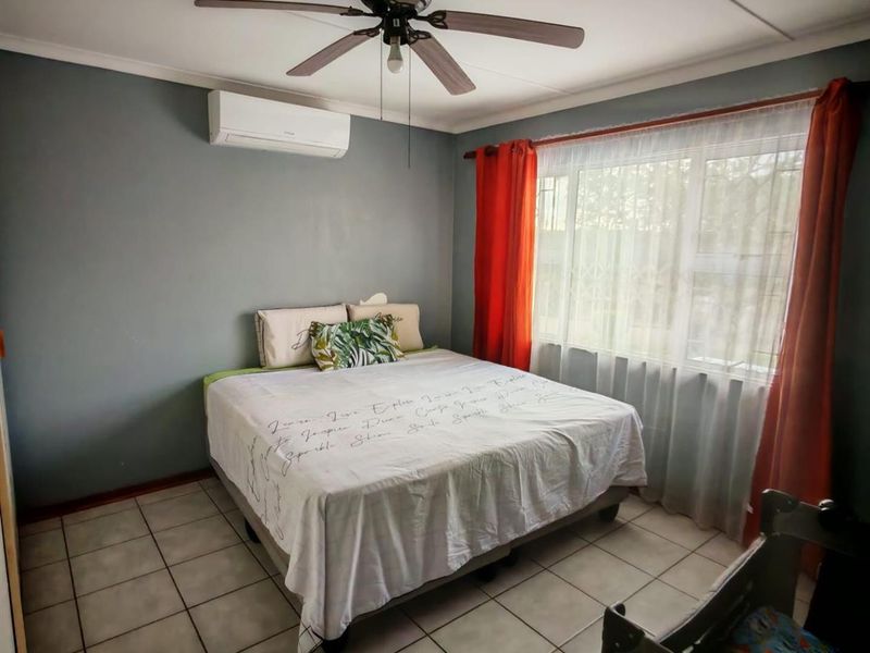A bedroom featuring tiled flooring, a ceiling fan, and a wall-mounted air conditioning unit, providing functional climate control and durable surfaces.