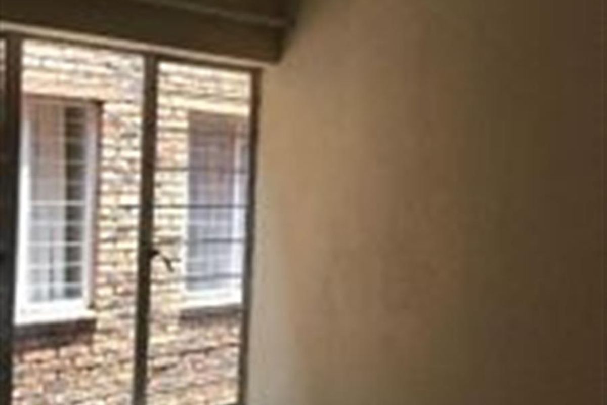 An empty bedroom featuring tiled flooring and a window fitted with security bars, requiring cosmetic updates to the wall finishes.