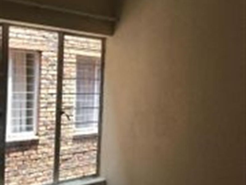 An empty bedroom featuring tiled flooring and a window fitted with security bars, requiring cosmetic updates to the wall finishes.