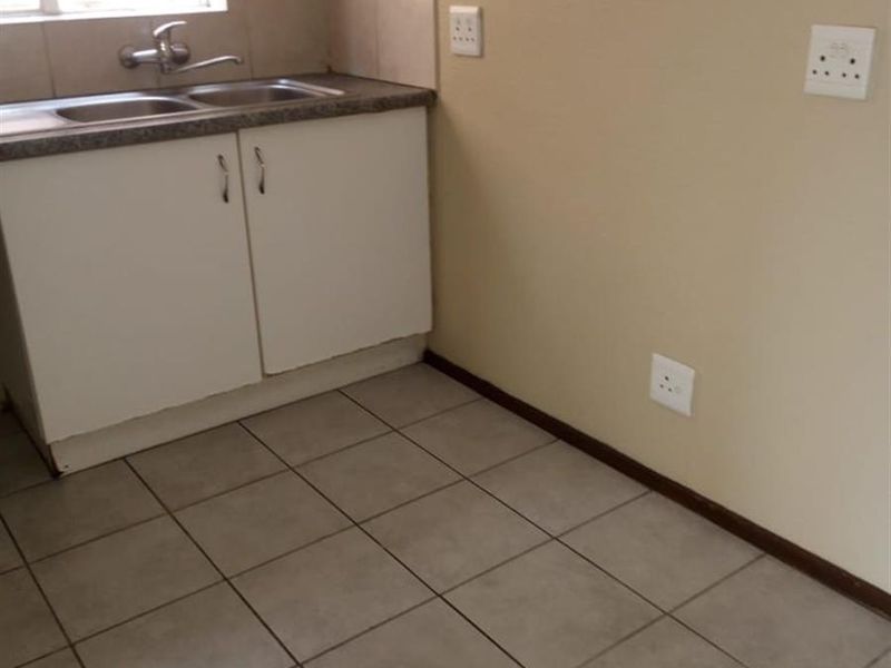 A compact, empty kitchen area featuring tiled flooring, a stainless steel sink with base cabinetry, and neutral wall finishes.
