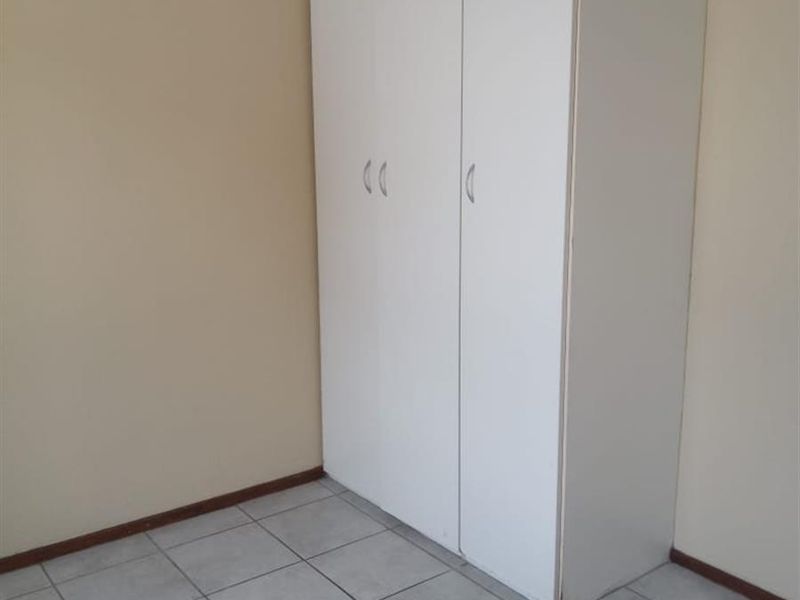 A simple, empty bedroom featuring neutral wall paint, tiled flooring, and a functional built-in wardrobe.