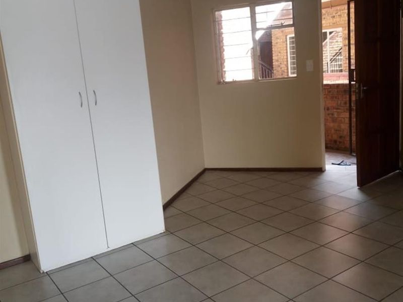 A clean, empty bedroom featuring neutral tiled flooring, a built-in white wardrobe, and natural light from the window.