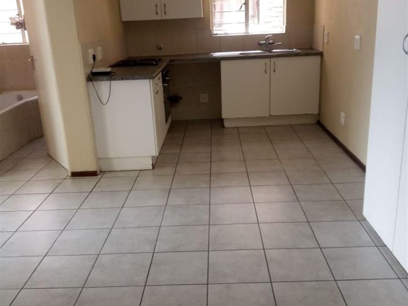 A functional kitchen featuring tiled flooring, built-in cabinetry, a stainless steel sink, and a hob, with an adjacent view into the bathroom area.