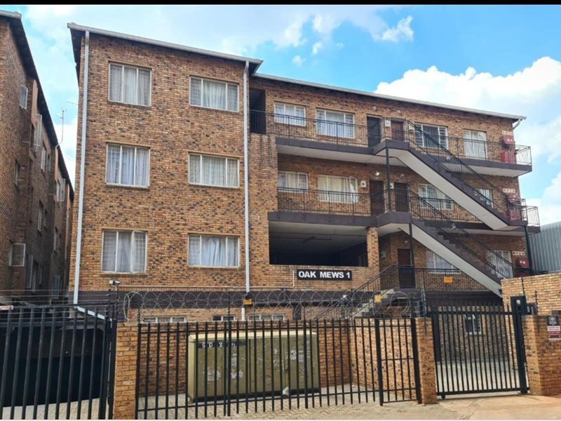 Exterior view of Oak Mews 1, a multi-story face brick apartment building featuring external staircases, balconies, and secure perimeter fencing.