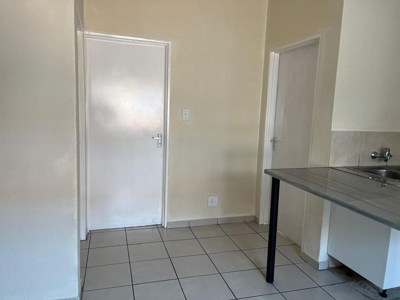 A functional kitchen area featuring tiled flooring, a laminate countertop with a stainless steel sink, and two internal doors.