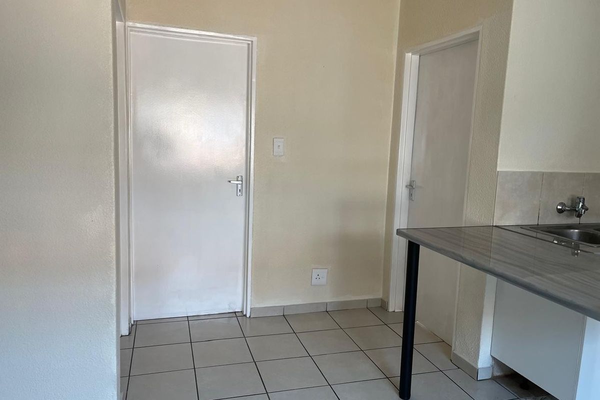 A functional kitchen area featuring tiled flooring, a laminate countertop with a stainless steel sink, and two internal doors.