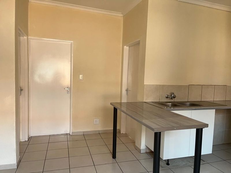 A functional kitchen area featuring tiled flooring, a stainless steel sink, and a breakfast bar counter, currently vacant and ready for updates.