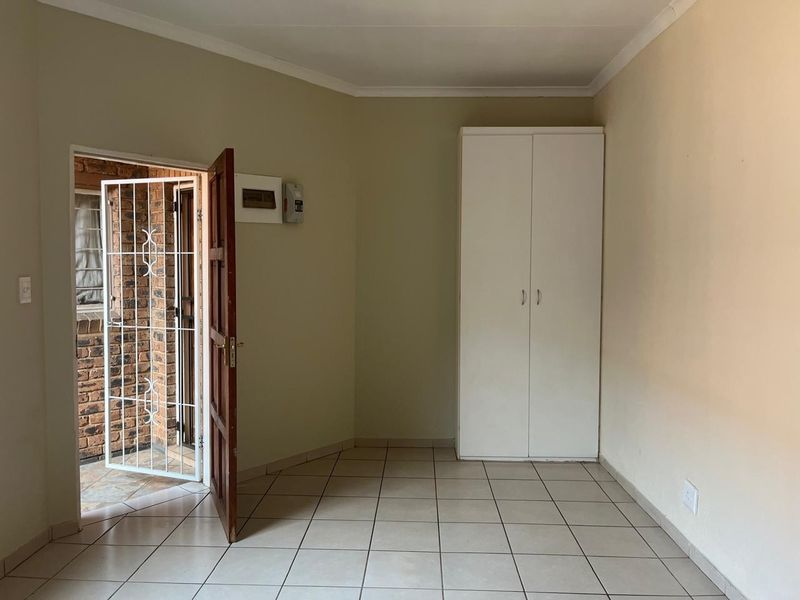 A clean, empty bedroom featuring tiled flooring, a built-in wardrobe, and direct access to an exterior area through a security gate.
