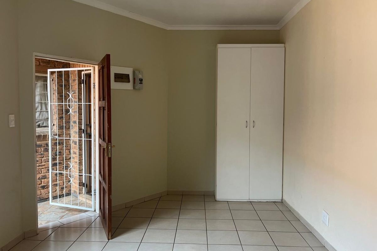 A clean, empty bedroom featuring tiled flooring, a built-in wardrobe, and direct access to an exterior area through a security gate.