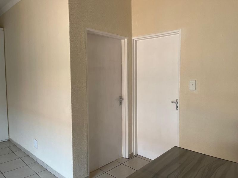A functional hallway area featuring neutral wall finishes, tiled flooring, and two internal doors providing access to adjacent rooms.