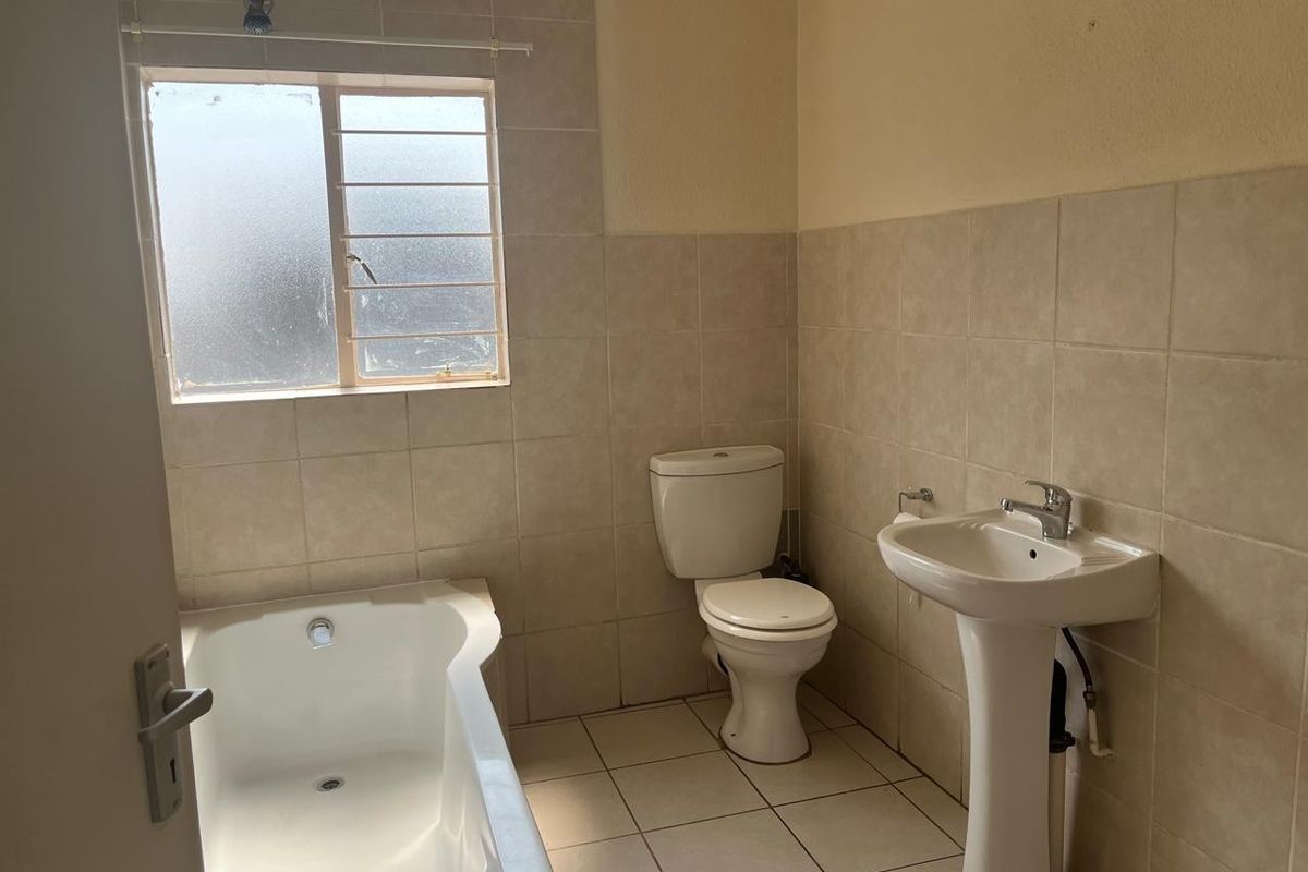 A functional bathroom featuring a pedestal basin, toilet, and built-in bathtub with neutral wall and floor tiling.