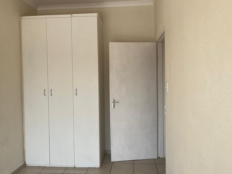 A simple bedroom featuring neutral tiled flooring and a white built-in wardrobe with an adjacent internal door.