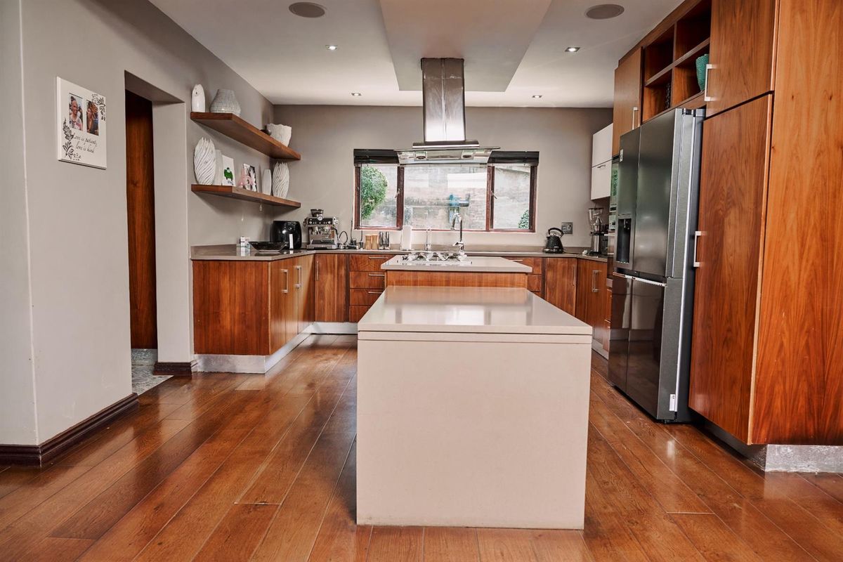 Modern kitchen featuring warm wood cabinetry, stone countertops, a central island, and integrated stainless steel extractor fan.