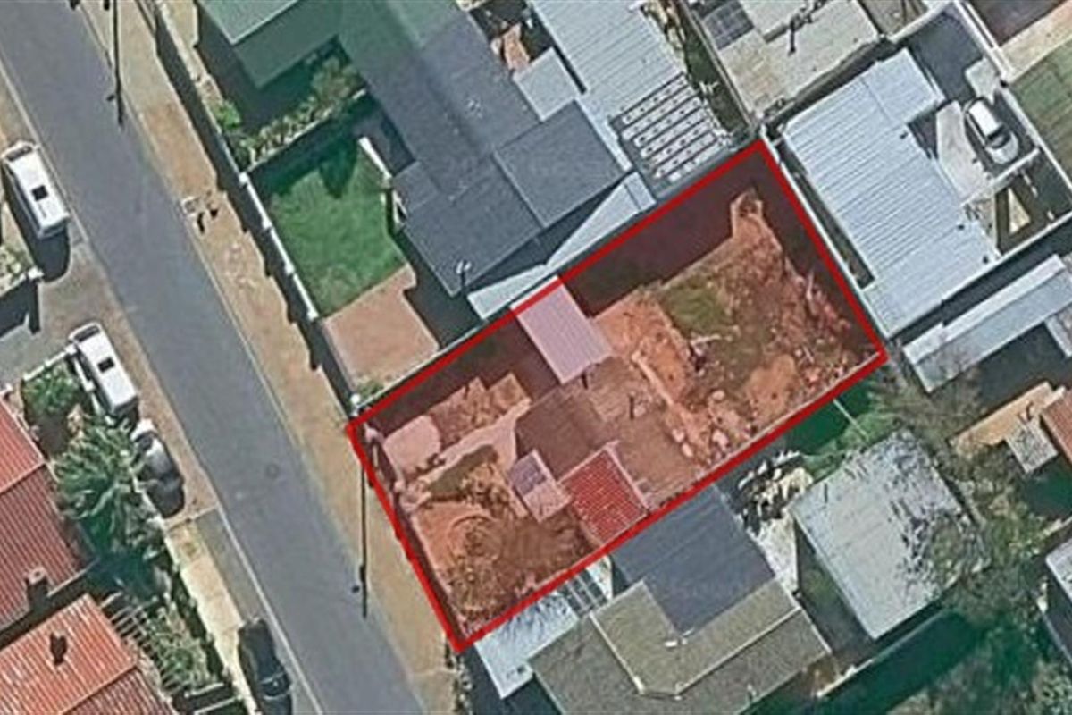 Aerial view of a vacant residential plot highlighted in red, showing undeveloped land with exposed soil and minimal existing infrastructure.