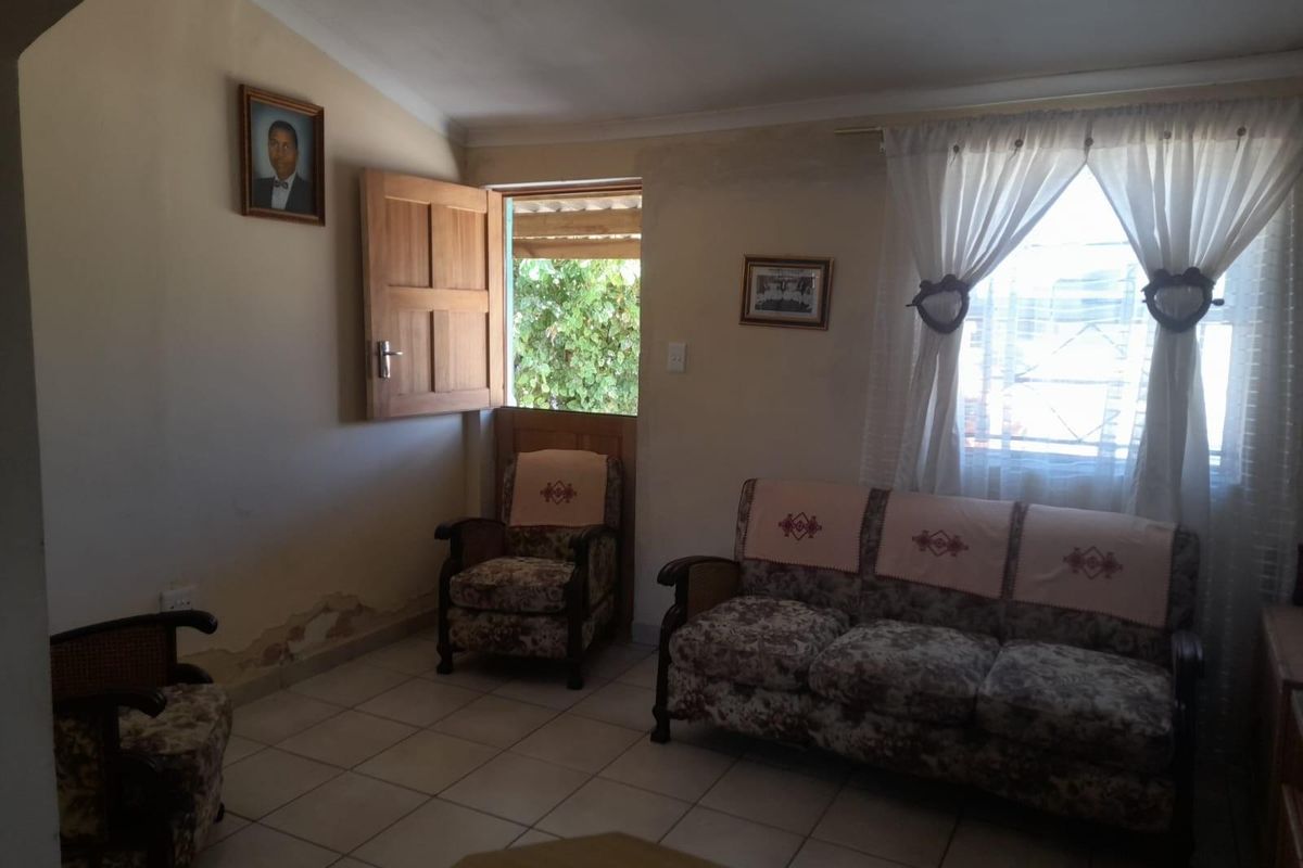A living room featuring tiled flooring, a wooden door leading to the exterior, and a window with curtains.