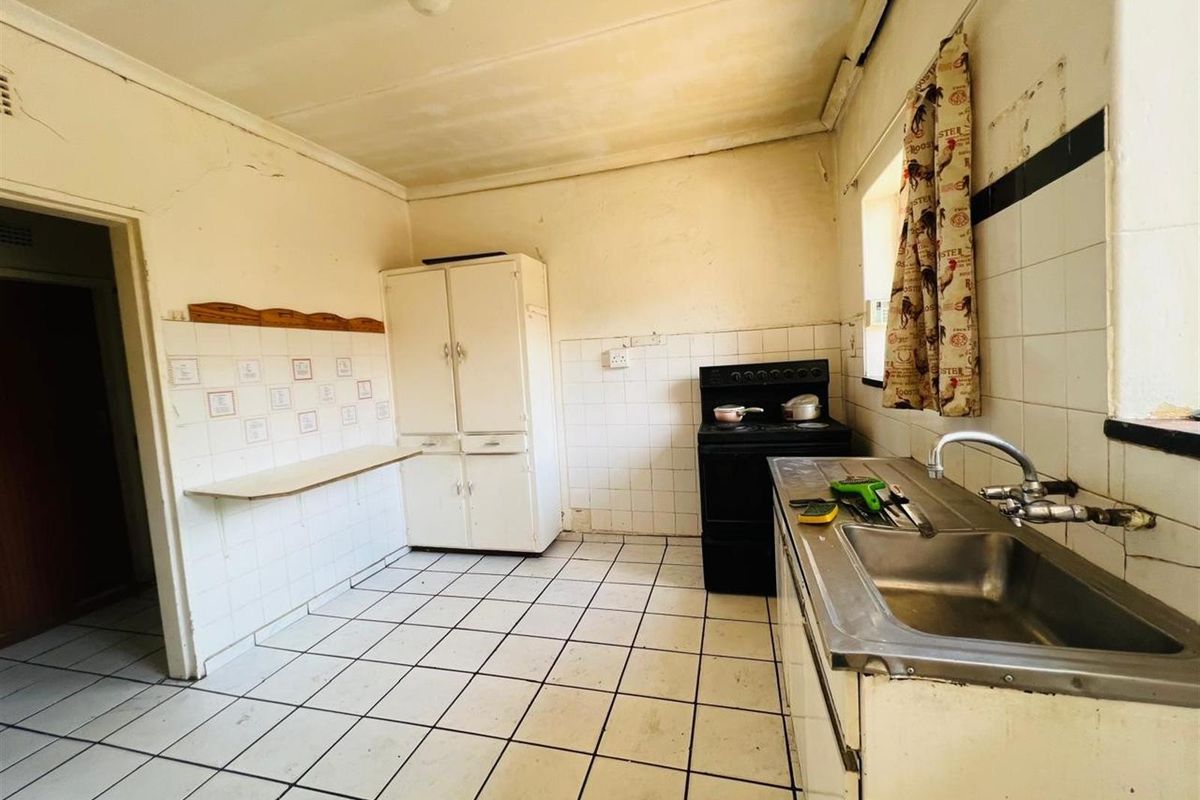 A dated kitchen featuring basic tiled splashbacks, a stainless steel sink, and built-in cabinetry, requiring significant renovation and cosmetic updates.