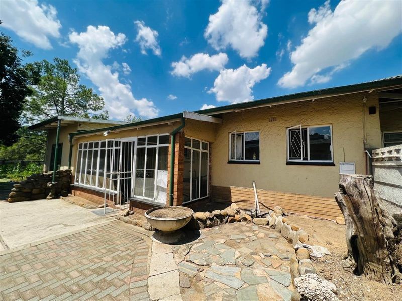 Rear exterior view of the property featuring a paved patio area, enclosed sunroom, and landscaped garden beds with stone retaining walls.