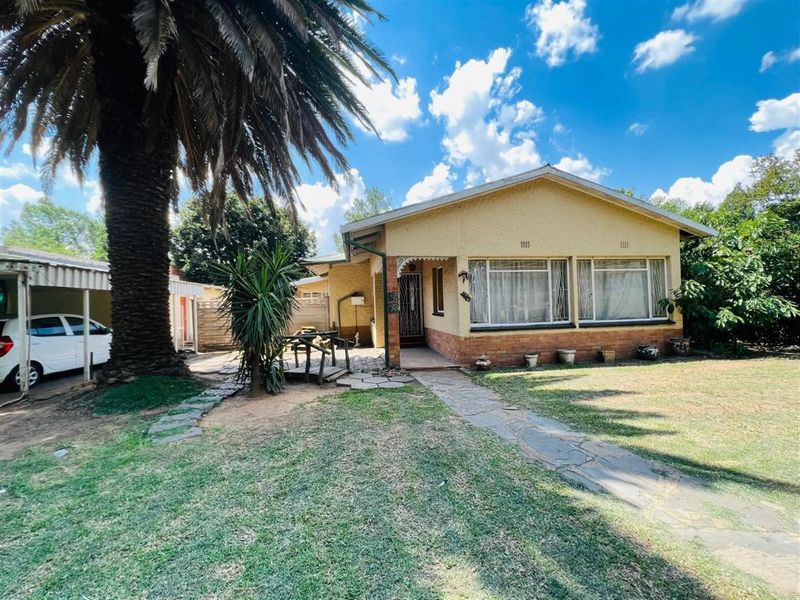 A single-story residential house featuring a yellow stucco facade, brick base, and a front garden with a stone pathway.