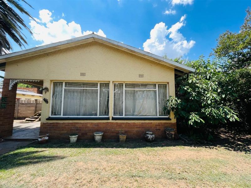 Front elevation of a single-story house featuring a brick base, stucco walls, and large windows with security bars.