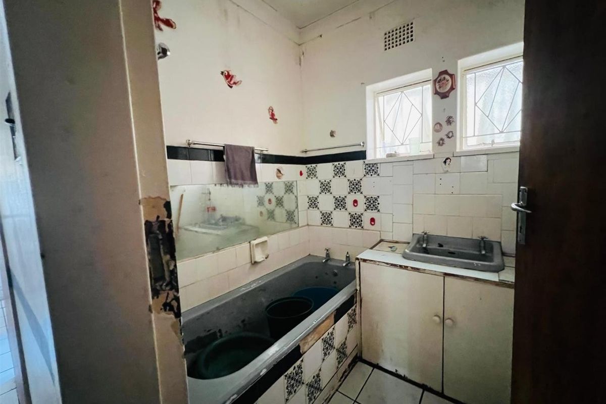 A dated bathroom featuring a built-in bathtub, vanity sink, and patterned wall tiling, requiring significant renovation and modernization.