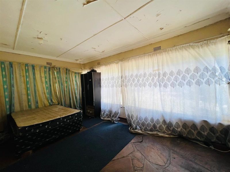A bedroom featuring stone flooring and large windows with curtains, requiring ceiling repairs and general refurbishment.