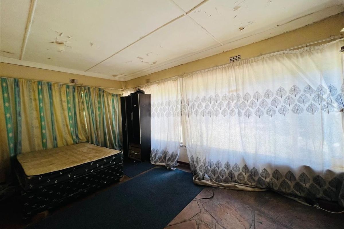 A bedroom featuring stone flooring and large windows with curtains, requiring ceiling repairs and general refurbishment.