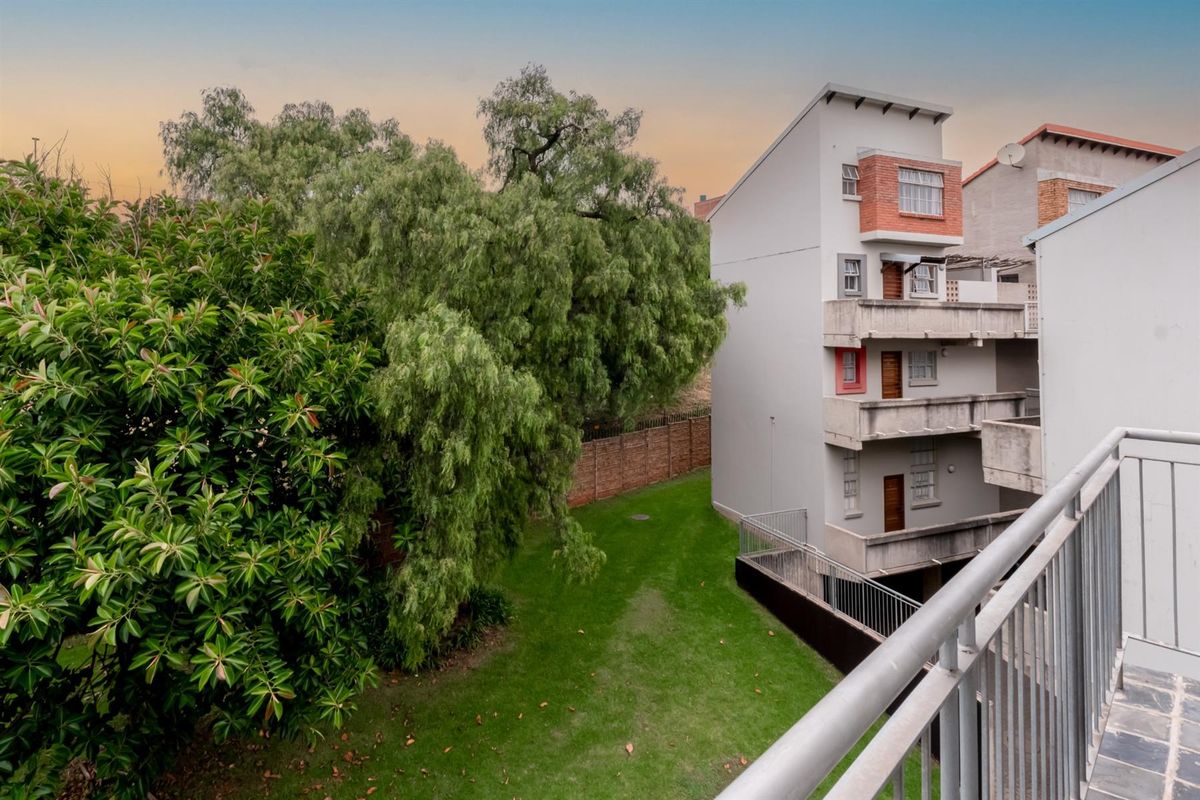View from a balcony overlooking a communal garden area and the rear facade of a multi-story apartment building.
