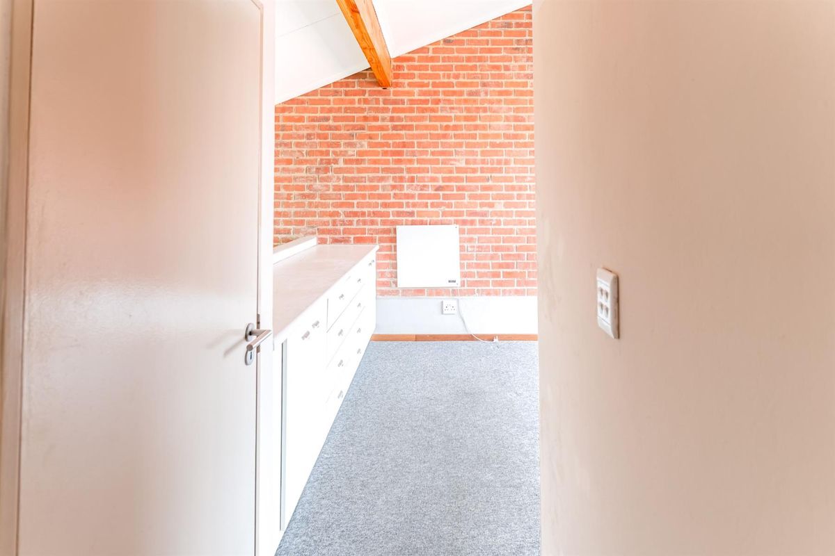 A bright bedroom featuring an exposed brick wall, timber ceiling beam, built-in storage cabinetry, and neutral carpeting.