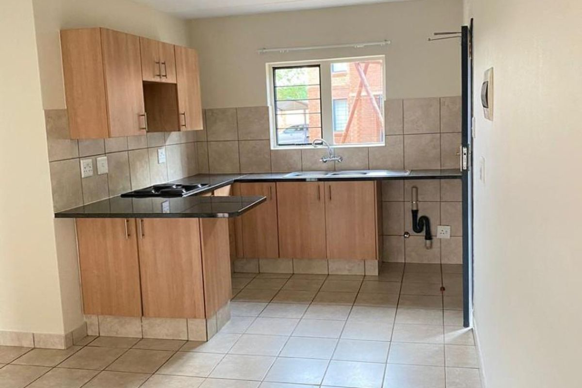 A functional kitchen featuring light wood cabinetry, dark countertops, tiled backsplash, and tiled flooring, with an open layout suitable for modern living.