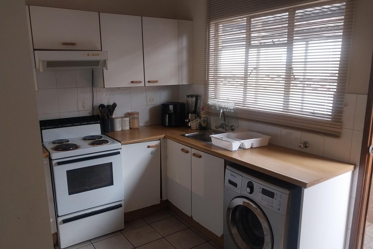 A functional kitchen featuring white cabinetry, wood-look countertops, a built-in extractor fan, and space for a washing machine under the counter.