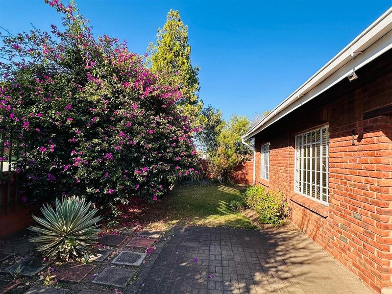 A private rear garden area featuring a paved patio, established landscaping, and a classic face-brick exterior wall with security-barred windows.