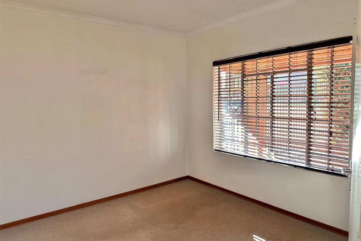 A vacant bedroom featuring neutral walls, carpeted flooring, and fitted wooden venetian blinds.