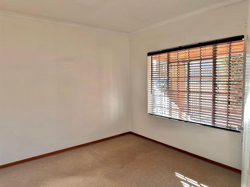 A vacant bedroom featuring neutral walls, carpeted flooring, and fitted wooden venetian blinds.