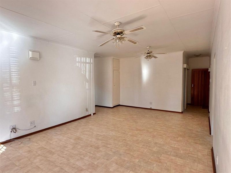 Spacious open-plan living area featuring tiled flooring, dual ceiling fans, and built-in storage cupboards.