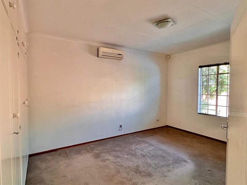 A spacious bedroom featuring built-in cupboards, a wall-mounted air conditioning unit, and a window with security bars.