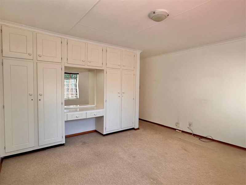 A bedroom featuring extensive built-in cabinetry with an integrated vanity and mirror, finished in a neutral tone with carpeted flooring.