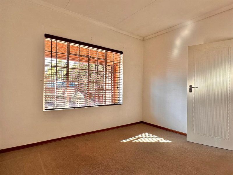 A vacant bedroom featuring neutral carpeting, a large window with fitted blinds, and a classic interior door.